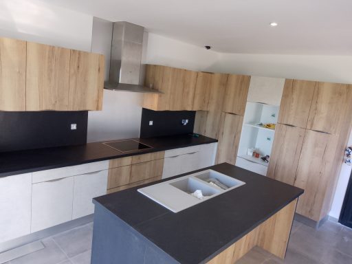 Cuisine moderne avec armoires en bois et plan de travail en noir, évier central.